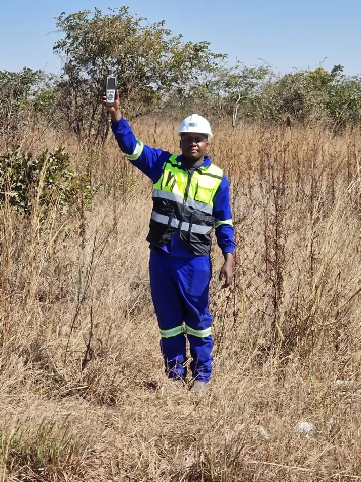 SunWise technician raising a handheld meter above tall dry grass on a transect path