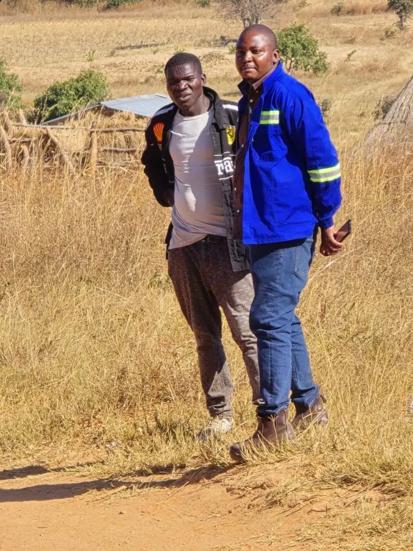 SunWise team member walking along a rural path with a resident, past reed and thatch structures