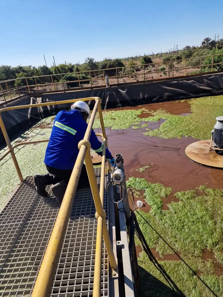 A SunWise technician taking a sample from a lined effluent treatment pond during an environmental monitoring visit