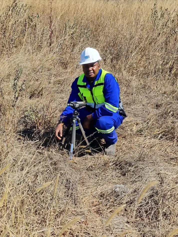 SunWise technician kneeling to set up a tripod-mounted monitoring instrument in open grassland