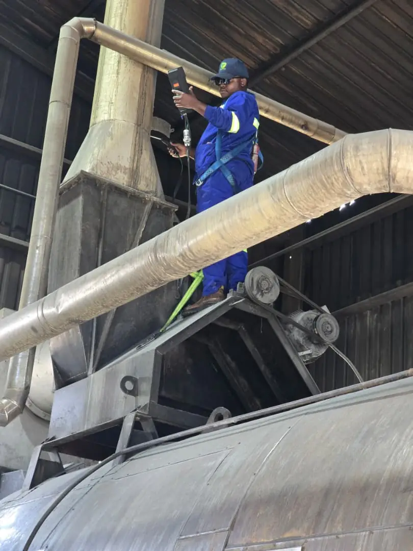 SunWise technician in a fall-arrest harness taking an emission reading on plant ducting at height