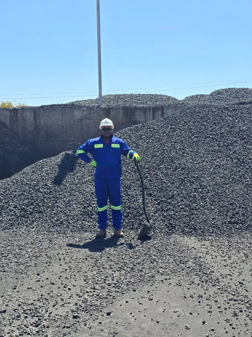 SunWise technician standing at the face of a large aggregate stockpile holding a sampling shovel