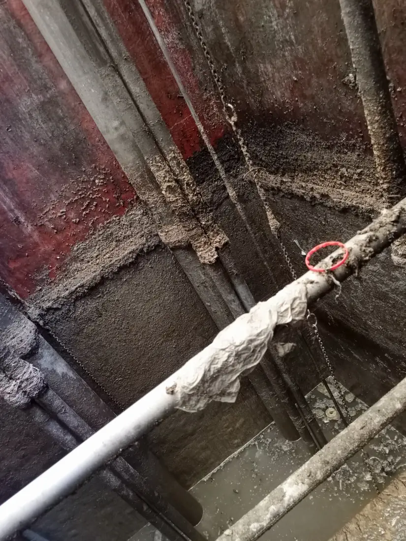 Interior of a steel storage tank showing residue on the floor and a lifeline rigged for confined-space entry