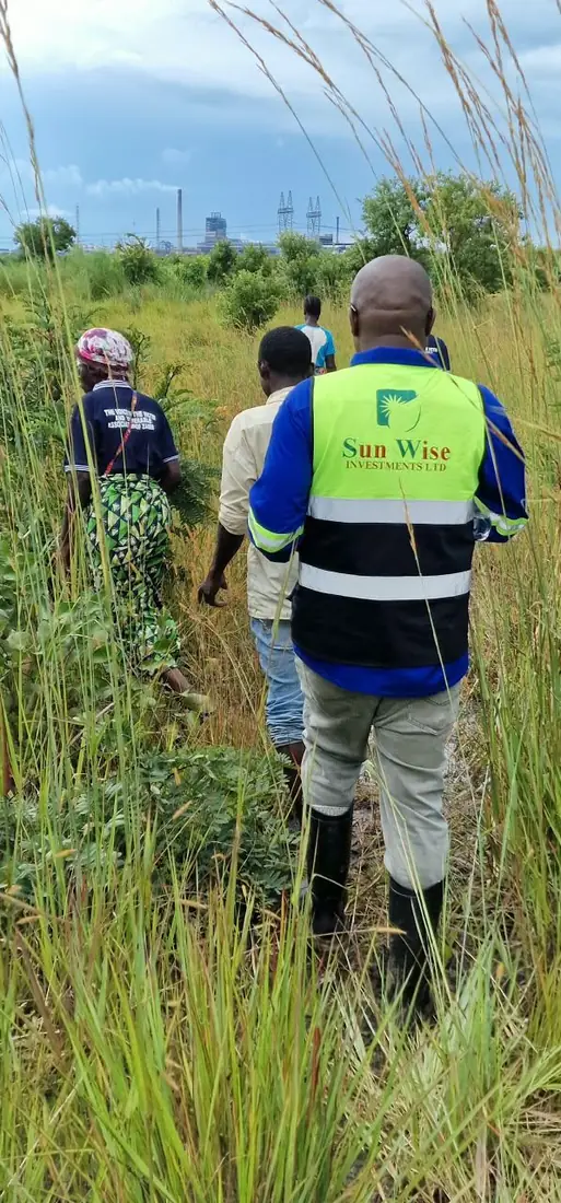 SunWise Investments Ltd team in branded high-visibility PPE walking a site transect, with industrial plant on the horizon