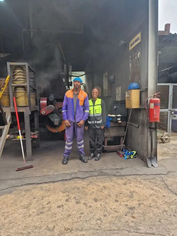 Two workers in protective coveralls and a high-visibility vest at the entrance of a smoke-filled workshop bay